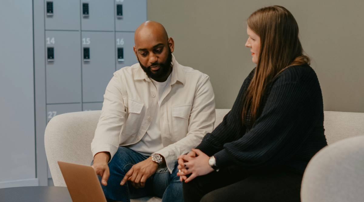 A man and a woman sit on a couch and talk as the man points at a laptop. You may want to hire a business consultant for expert help in facing challenges such as a company transition or stagnant growth. 