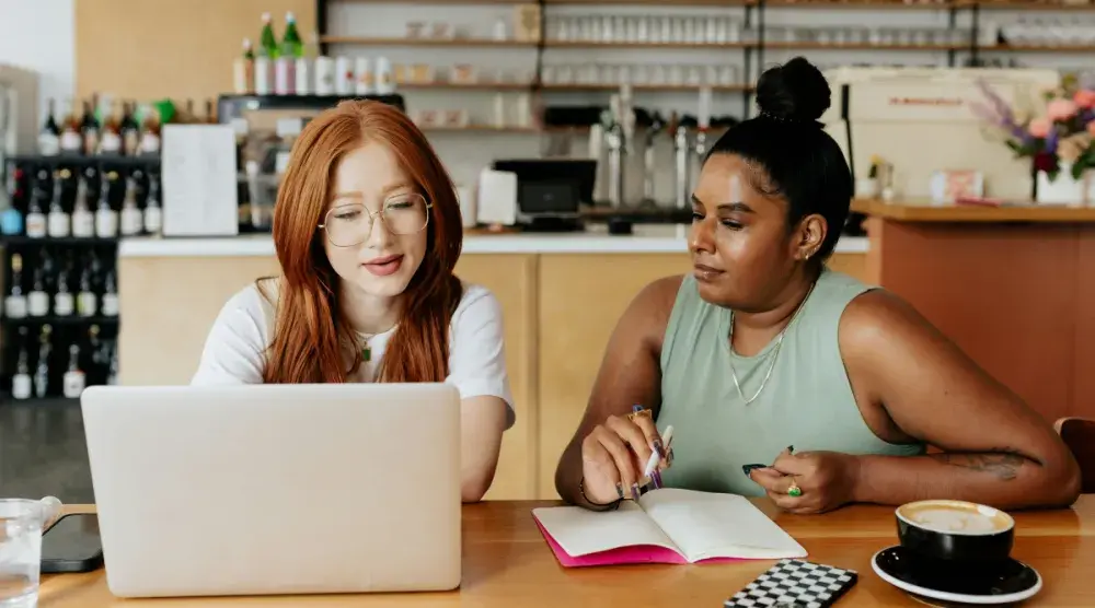 Two female Nebraska business partners sit together at a laptop and conduct a Nebraska business search.