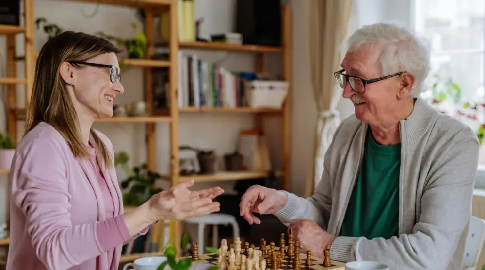 A woman and an elderly man play chess in his living room. Avoiding the probate process can save money, speed up the transfer of assets to beneficiaries, and preserve family privacy.