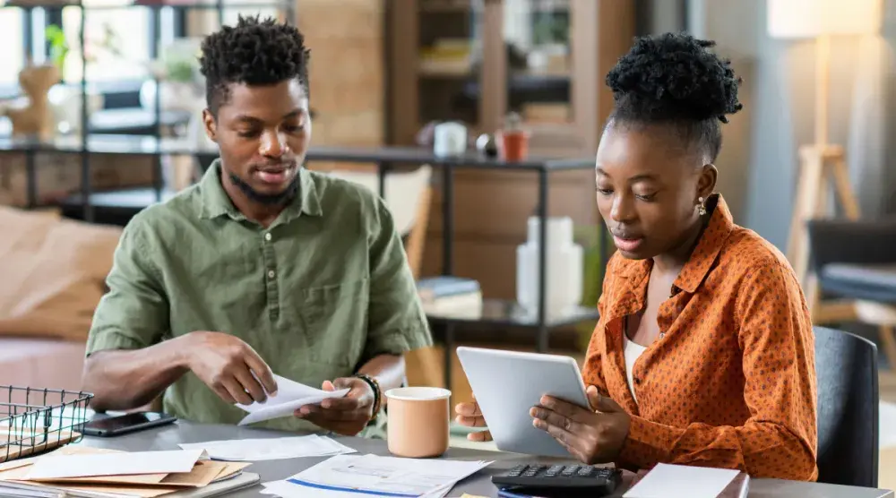 A man and a woman sit at a table going over paperwork with a calculator. Finding out if a business name is available is a crucial step in starting a business in Indiana.