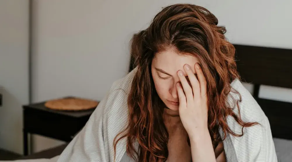 A young woman sits at a desk with her head resting in her hand as she thinks about why she shouldn't be her own registered agent. 