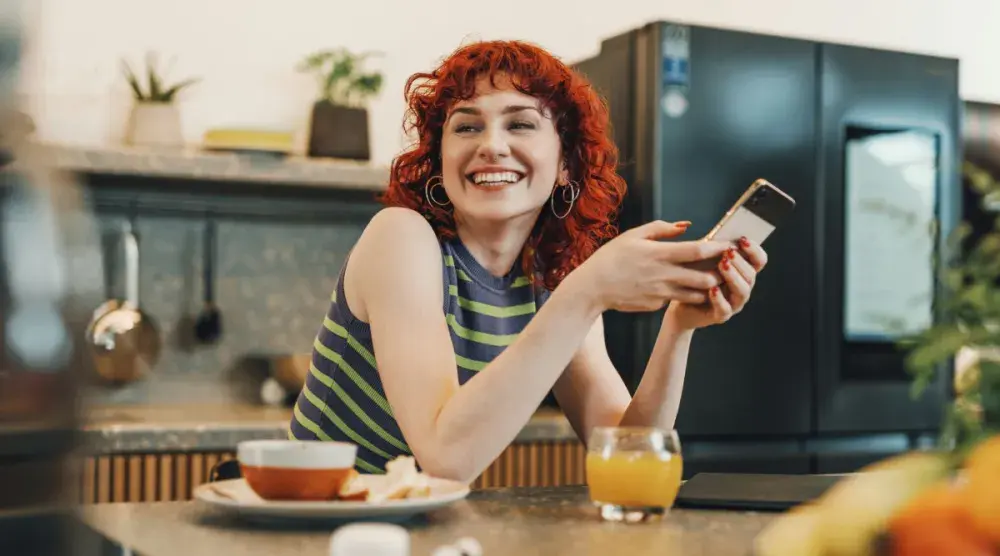 A young woman who runs an LLC out of her Nebraska home checks her cellphone during breakfast in her kitchen. This guide can help you form your Nebraska LLC.