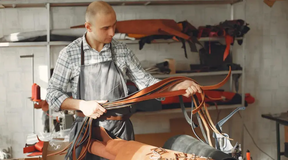 An leatherworker measures the sizes of a stack of belts.