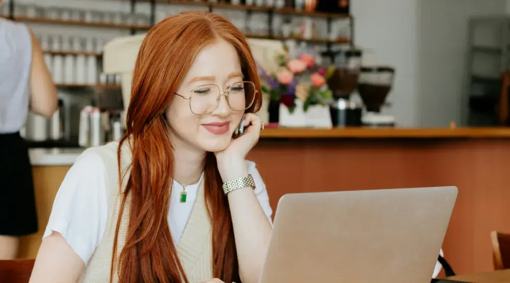 A woman sits in a coffee shop working on her computer and researching in-kind donations. There are two types of in-kind donations: goods and services.