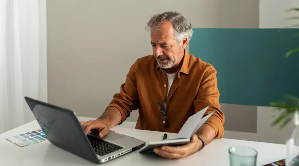 A California man fills out online forms for creating a living trust at his laptop while holding an open notebook in one hand.