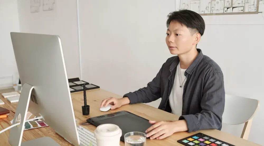 A brand consultant sits at their desk and uses their computer to work on a design project.