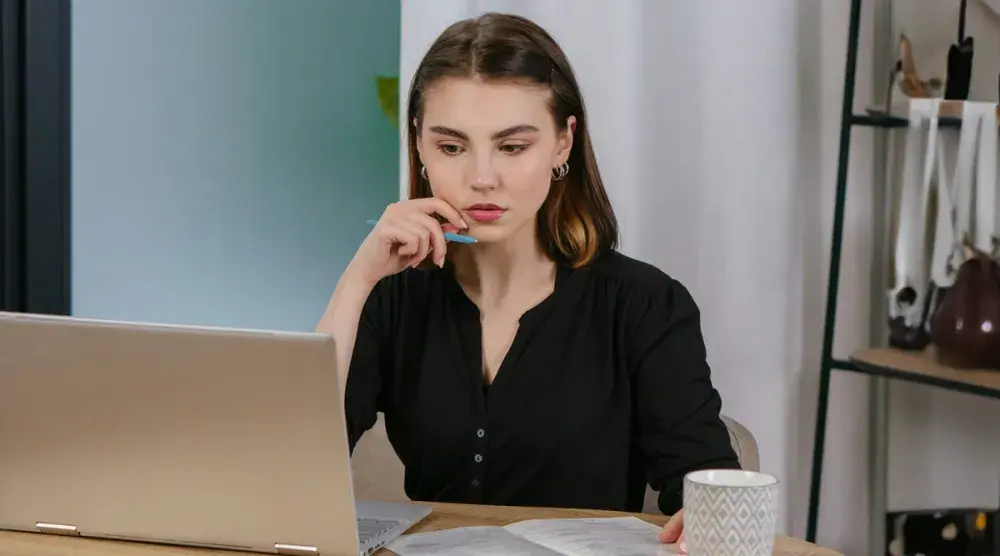 A woman sits at a desk on her laptop and carefully reads the arbitration agreement in a contract she is about to sign.