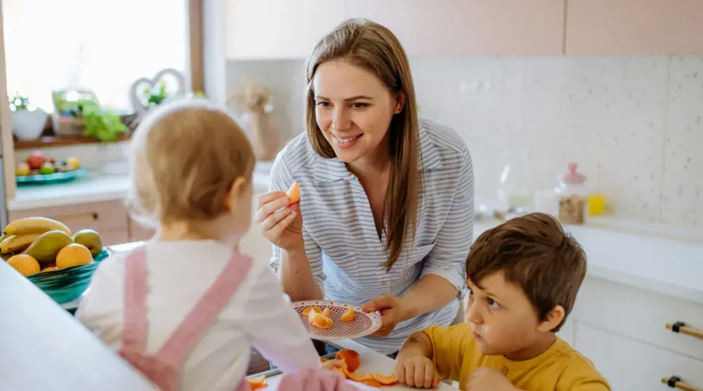 A Georgia woman feeds a baby in a high chair while her toddler stands next to her looking on. If the beneficiaries of your living trust are children, then you can specify what age you want them to receive full control of these assets and under what terms.