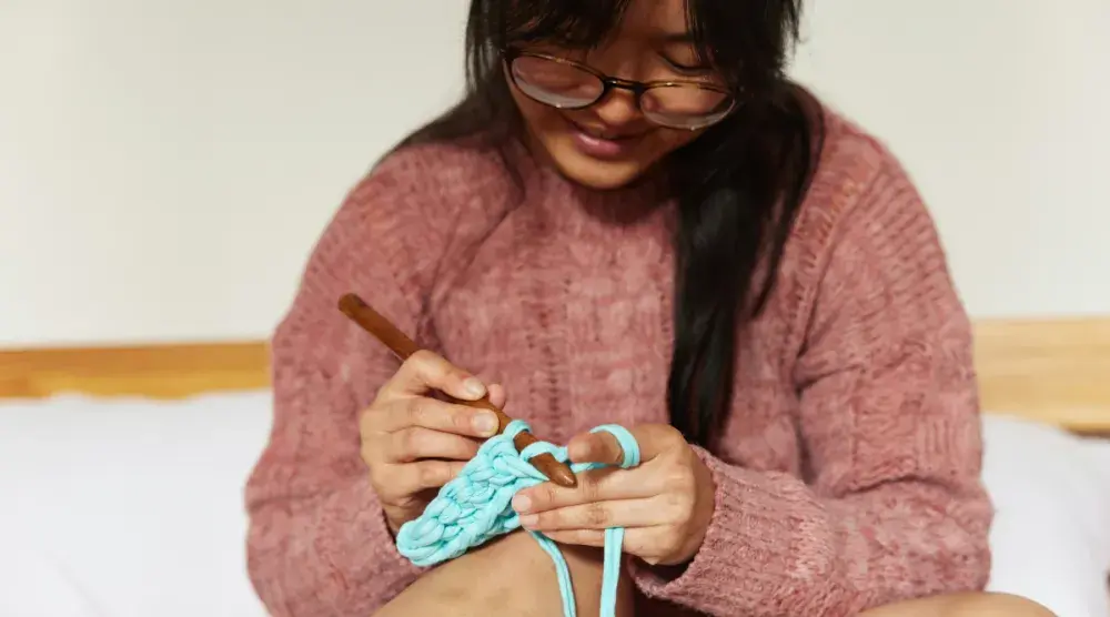 A woman smiles as she knits.