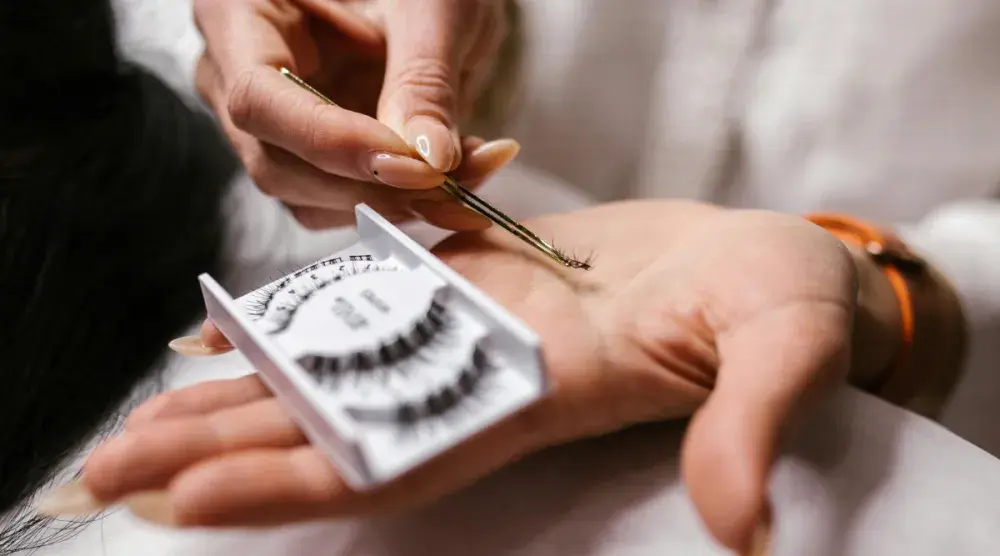 Close up of an aesthetician's hands as they use precision tools to pick up a set of lashes from a tray.