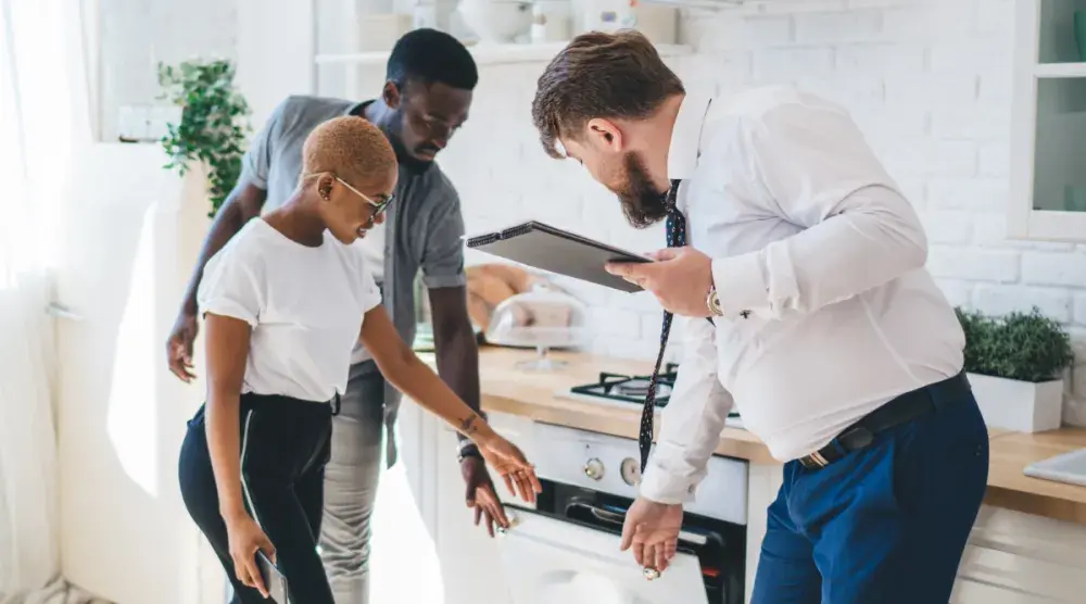 A man and woman look inside a dishwasher as a real estate agent holds it open. Choosing the right name can be critical in ensuring your real estate business stands out among such steep competition.