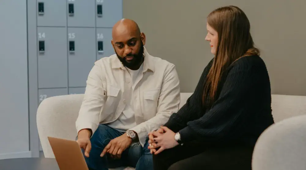 A lawyer and his client sit on a couch. She listens intently as he points at a laptop and they talk through her wrongful termination case.