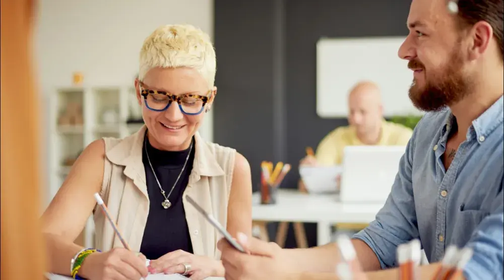 A woman and man seated at a table fill out their applications to copyright their poetry.