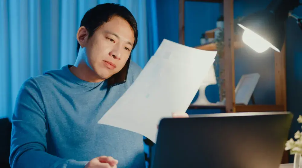 A man sits at his desk and sorts through business records while filling out his California statement of information.