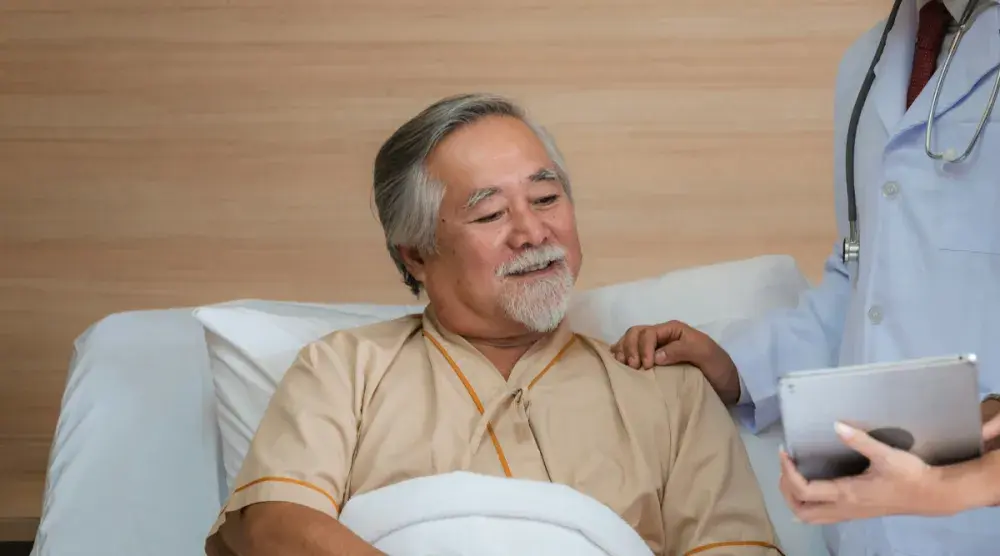 A man in a hospital bed reviews his power of attorney with a hospital administrator before a surgery.