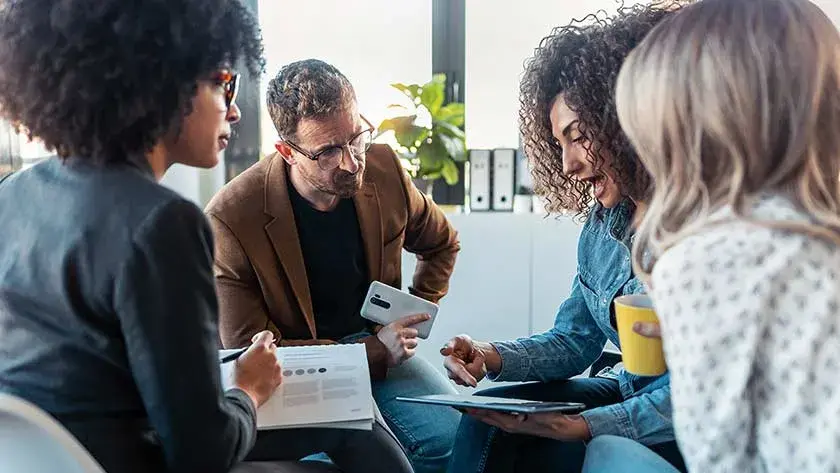 Four business colleagues, three women and a man, sit together closely as they discuss a proposal.