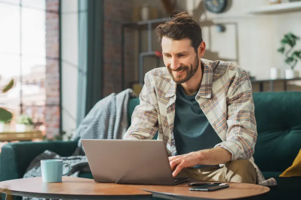 A man seated on a couch reads about cash vs. accrual accounting on his laptop.