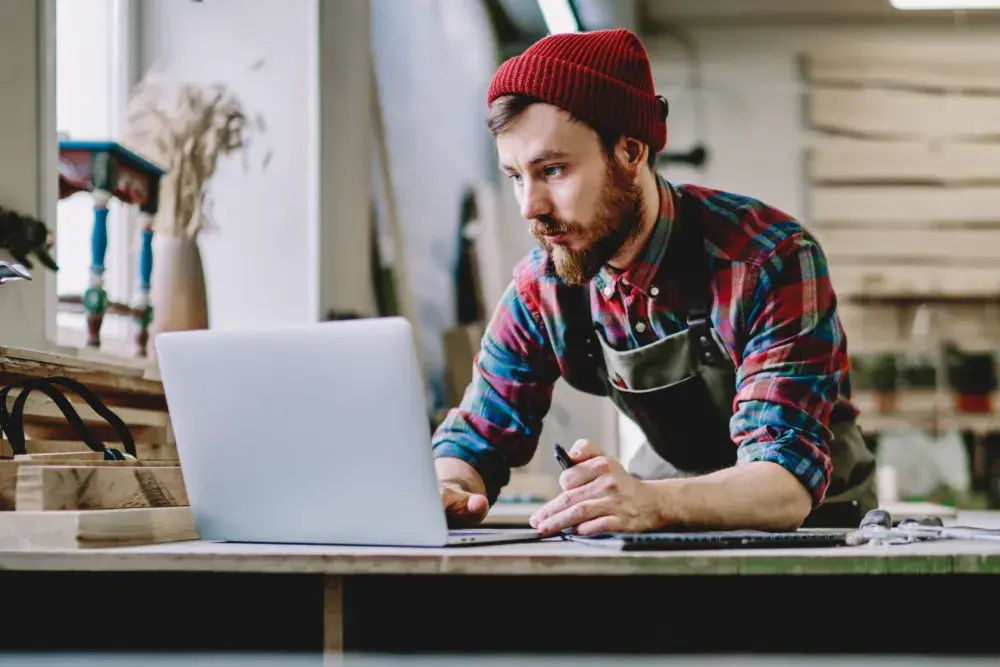 A man wearing a red hat looks at his open laptop in his workshop. Your Delaware corporation name is how customers identify your company.