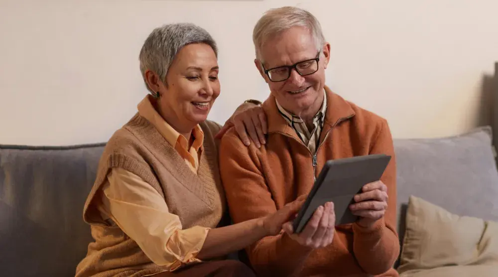 An older woman and man, seated on a couch, look for a postnuptial attorney on their tablet. Your postnuptial agreement should be as unique as you and your spouse. 