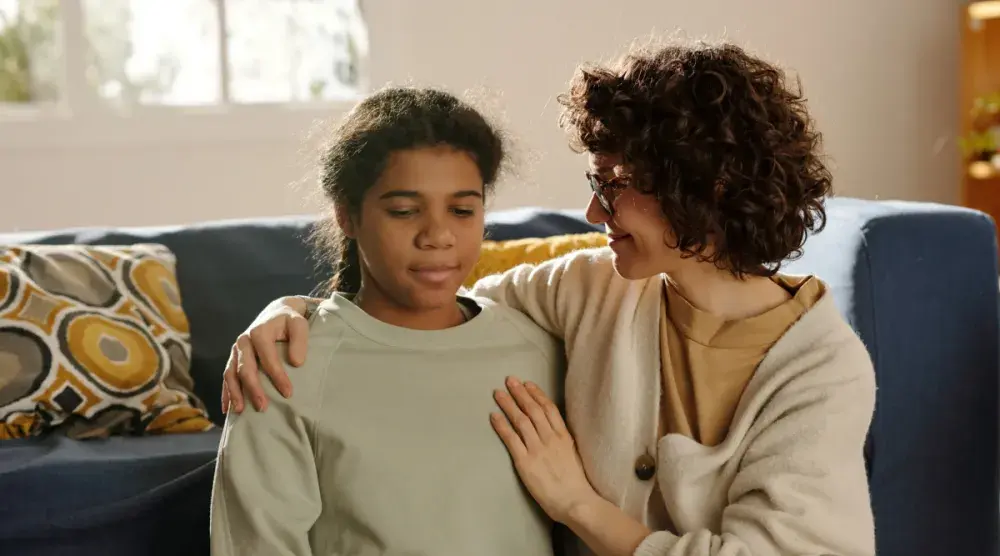 A young girl is embraced by her mother as they sit on the couch. If a parent dies without a will, where the child lives determines what she is entitled to. 