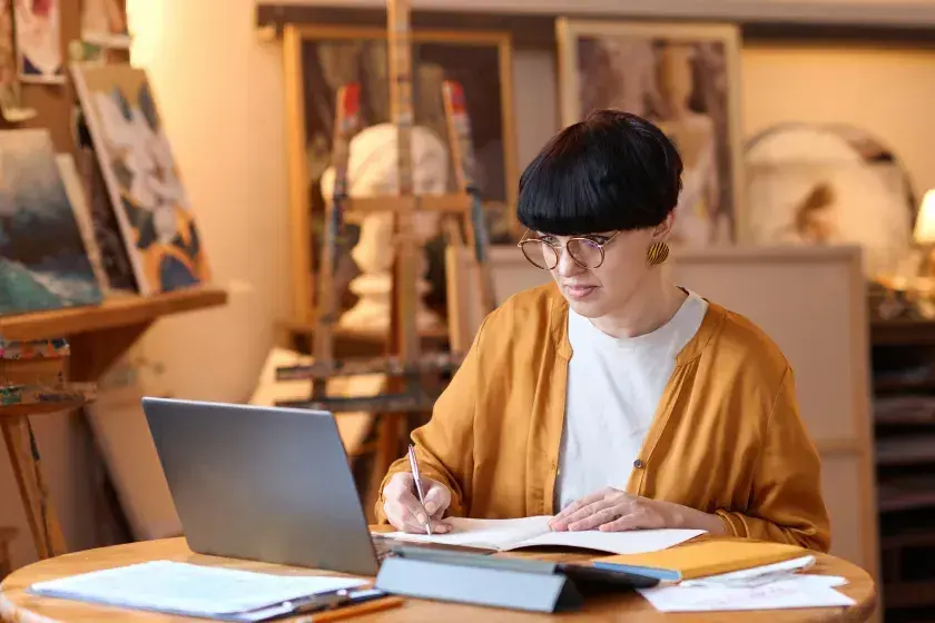 A small business owner seated at a table takes notes while looking up guidelines for termination letters on her laptop computer