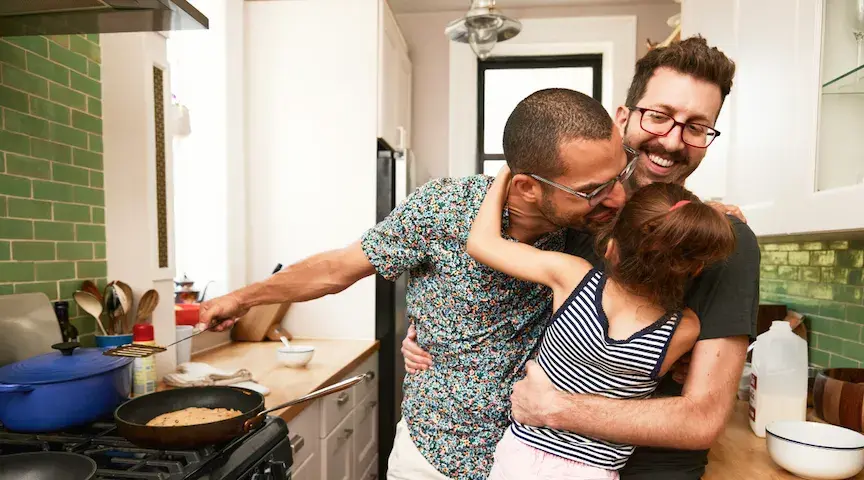 Two men who are domestic partners embrace their child and each other in their kitchen. A domestic partnership is a legally recognized, committed relationship that is an alternative to marriage.