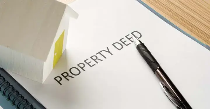 Origami house and pen lying on a notebook with the words "property deed" printed on the cover