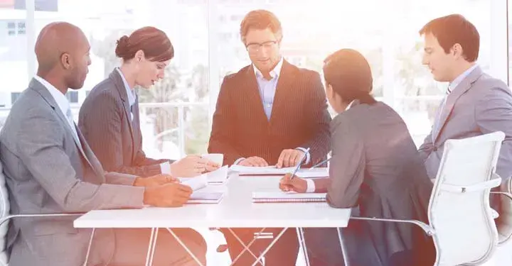 Businesspeople gathering around white table and taking notes 