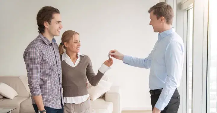 Couple in living room given set of keys by man in button-down shirt