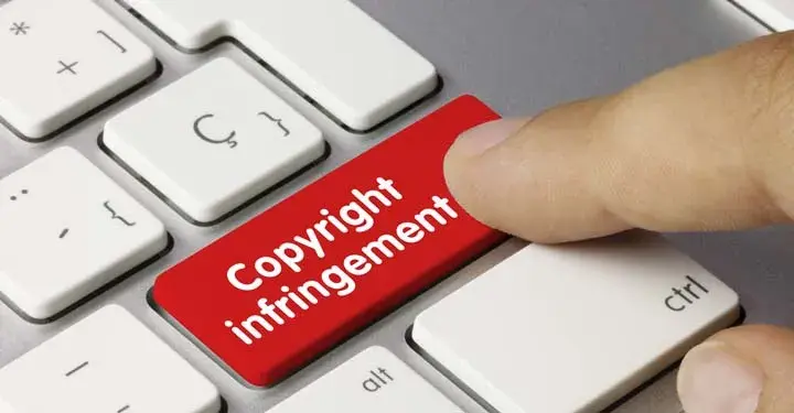 Finger pressing red button on computer keyboard with white text "copyright infringement"