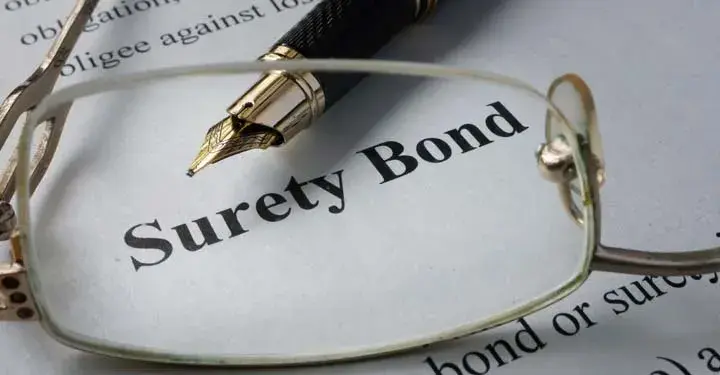 Wireframe glasses lens resting on paper and magnifying the words "surety bond" and tip of fountain pen