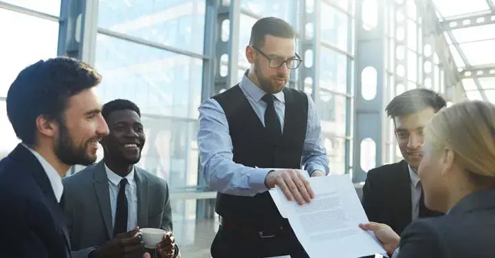 Businessman in group of businesspeople hands businesswoman paper