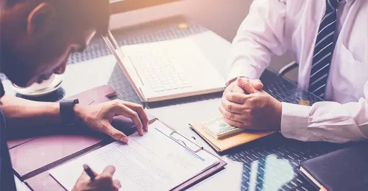 Man signing form across from businessman