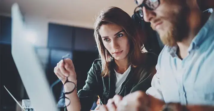 Man wearing glasses and woman holding a pair of glasses looking at a laptop together