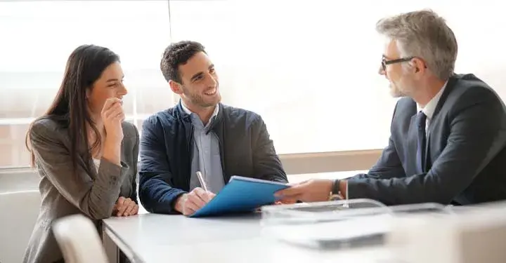 Two brunettes sign document while smiling at businessman