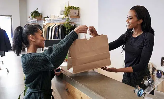 A female employee handing a paper bag to female customer in a clothing shop