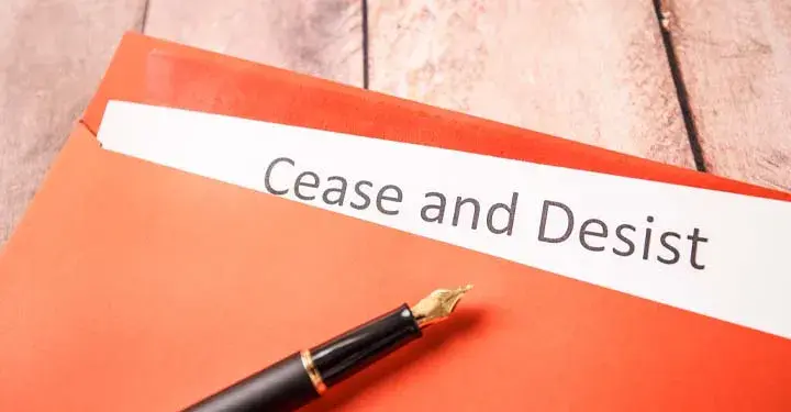 Fountain pen on orange folder containing paper with title "cease and desist" printed on it