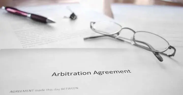 Glasses, pen, and binder clip on papers focusing on text "arbitration agreement"