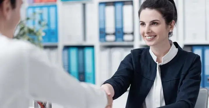 Businesswoman smiling and shaking hand of businessman while in front of shelves of binders