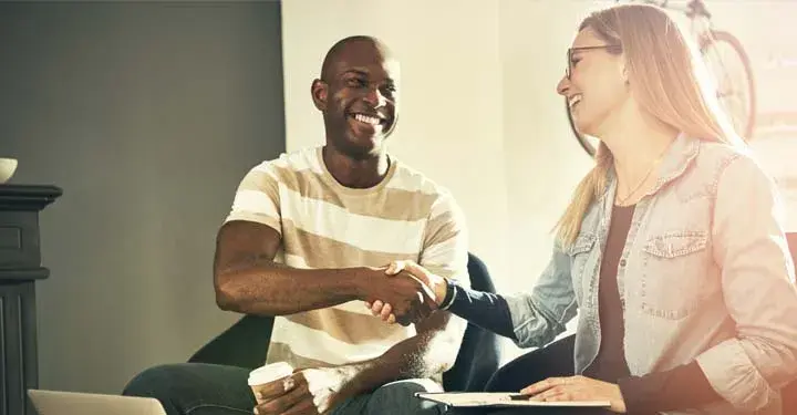 Casually dressed man and woman shake hands while sitting in coffee shop in front of laptops