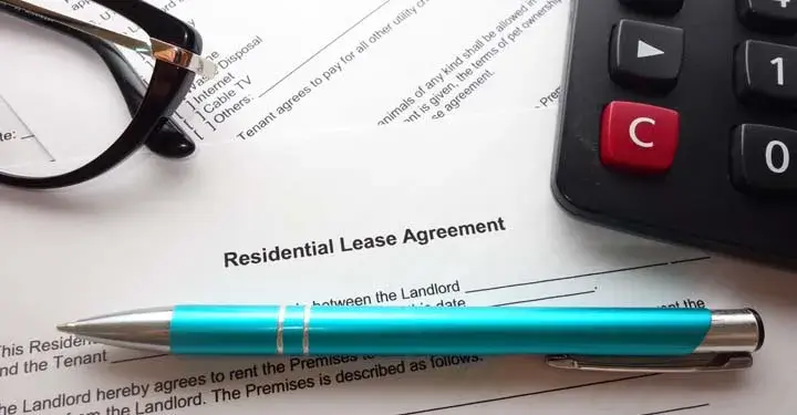 A pair of glasses, a blue ballpoint pen, and a calculator resting on a residential lease agreement