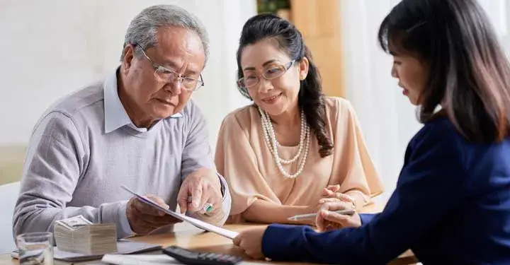 Older couple gestures to papers handed to them by businesswoman