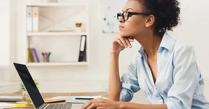 Woman typing in office while wearing black glasses and resting her chin on her hand