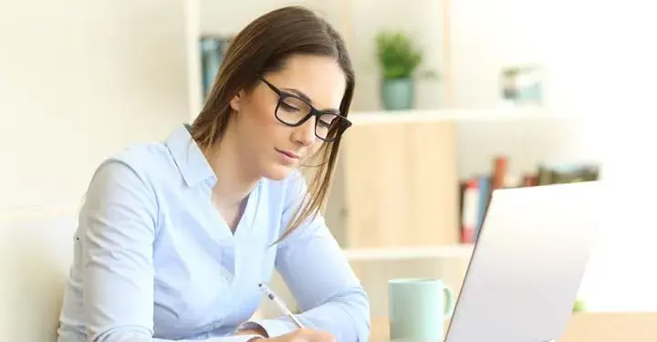 Businesswoman in glasses with long hair writing with ballpoint <a href=