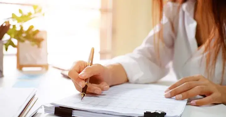 Woman at desk with fountain pen looking over papers