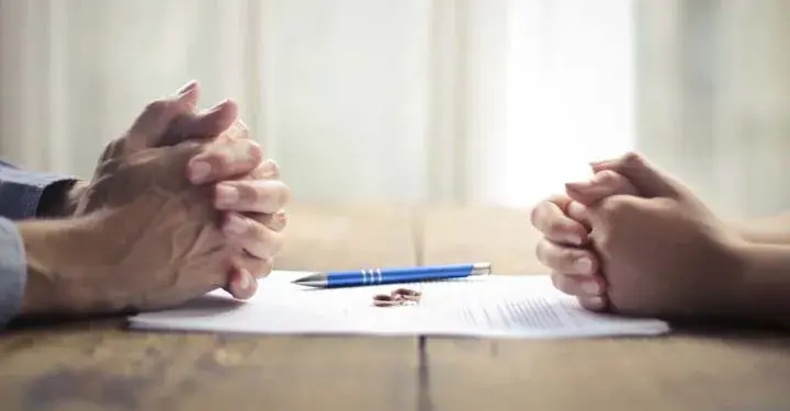 Men and women's hands on opposite sides of paper with wedding rings and pen resting on it