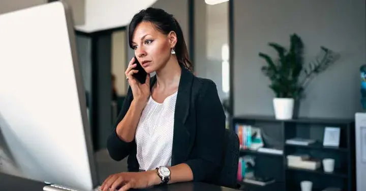 Businesswoman in an office talking on a cellphone and using a desktop