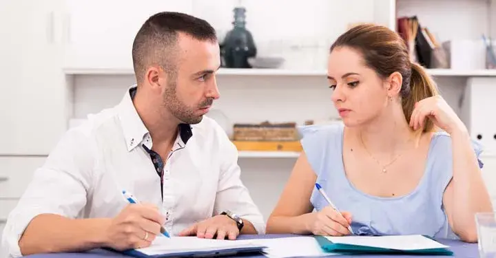 Man and woman sadly looking at each other while they hold ballpoint pens over forms