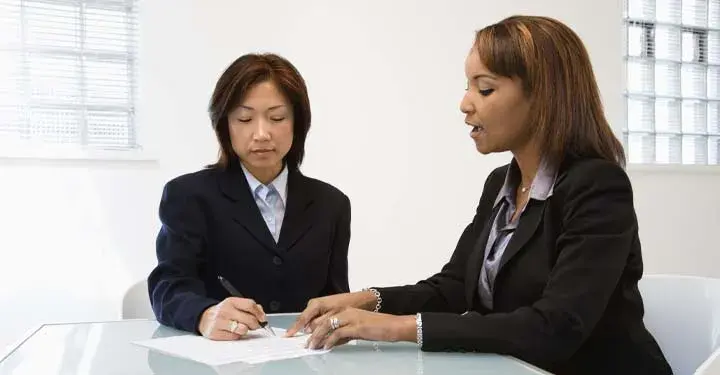 Two businesswomen sitting at a table reviewing a document