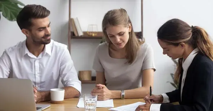 Three businesspeople sitting at a table watching as one writes something down